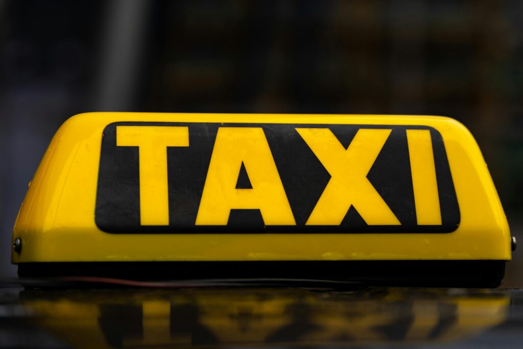 Illuminated taxi sign on top of a car at night representing costly transport option compared to public transit