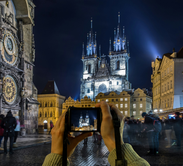 Visitor photographing Old Town Square Prague at night with the Astronomical Clock and Church of Our Lady before Týn in the background