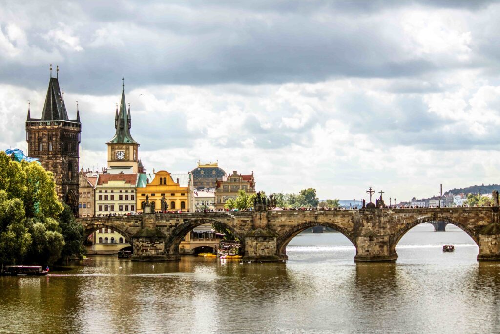 Charles Bridge crossing the Vltava River with Old Town towers and historic Prague skyline under dramatic clouds.