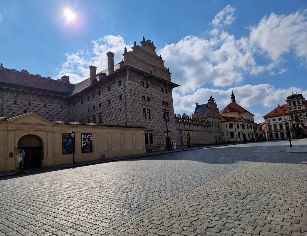 Quiet courtyard area near Prague Castle with historic Renaissance buildings, cobblestone square, and soft afternoon sunlight in Prague, Czech Republic, showing the peaceful atmosphere away from the crowded main areas.
