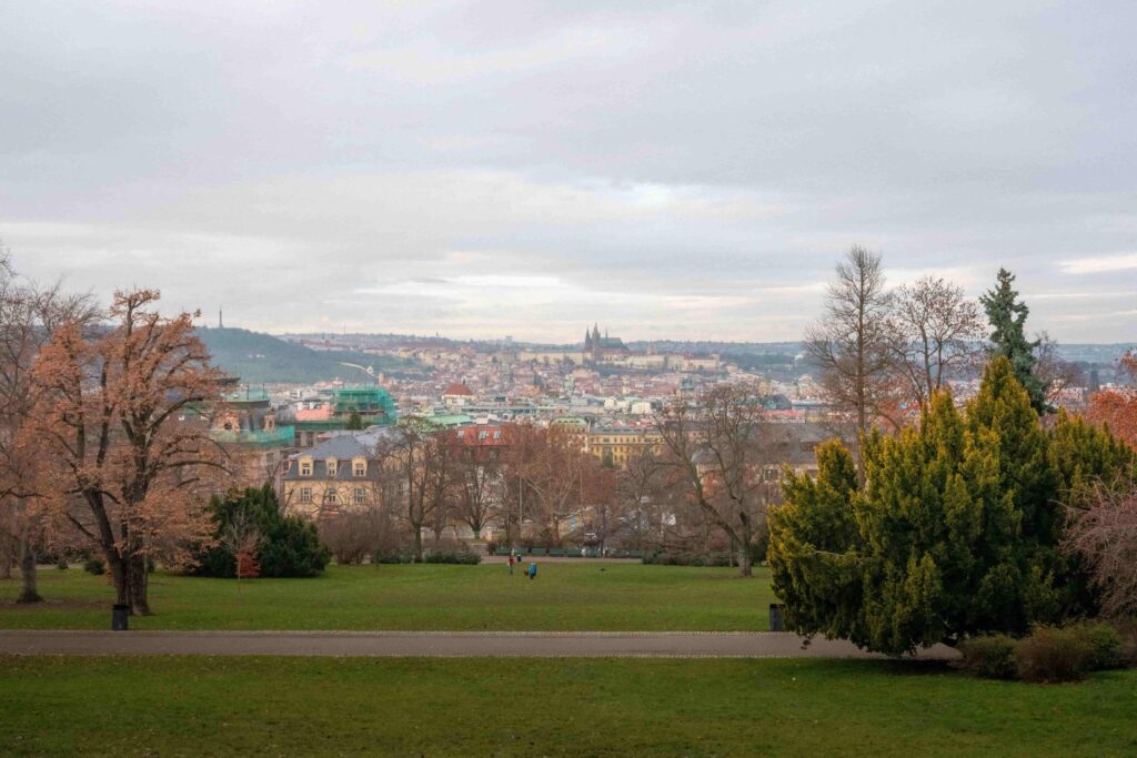 Panoramic view of Prague from Letná Park with green lawns, mature trees, and the city's historic skyline in the distance