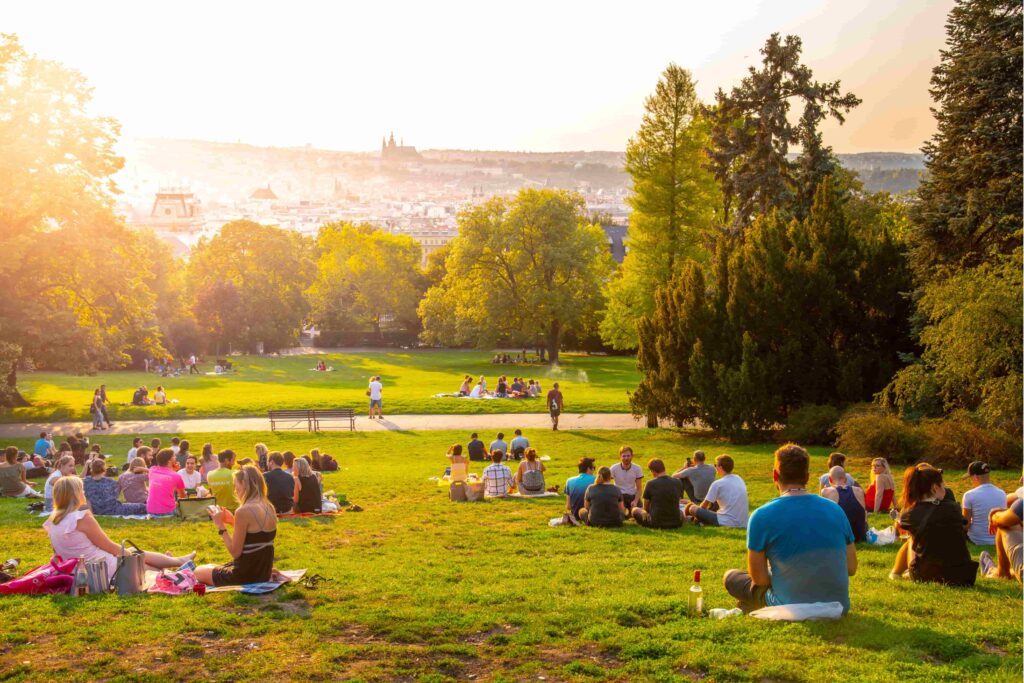 People relaxing on the grass beneath mature trees in Kampa Garden, a peaceful riverside park on Kampa Island in Prague, Czech Republic.