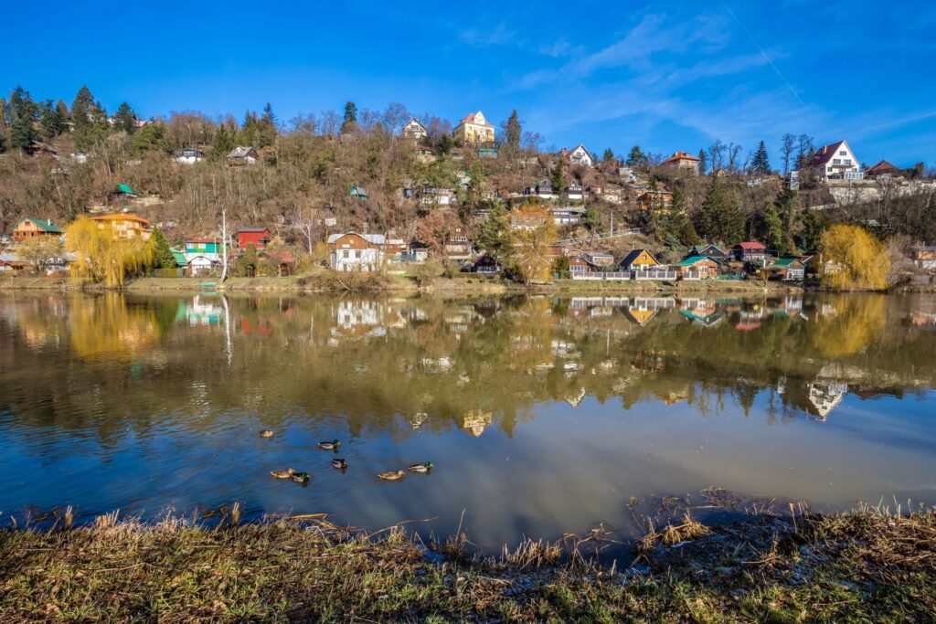 A view of the Berounka River, one of the Prague rivers, with riverside homes reflected in the water.